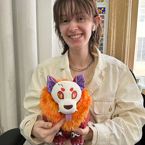 A woman holds the plush hellhound. It is slightly larger than her head.
