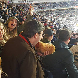 A man pretends to eat the plush hot dog toy. It is about the size of his head.