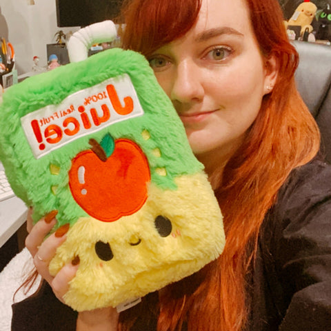 A woman holds the plush juice box up to her face. It is slightly larger than her head.