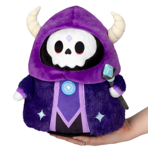 A plush toy designed as a mini lich with a purple hooded robe, white skull face, and holding a blue staff.