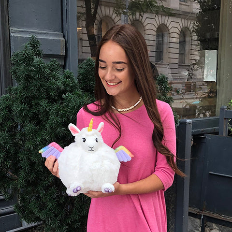 A woman holds the plush llamacorn toy. It is slightly larger than her head.
