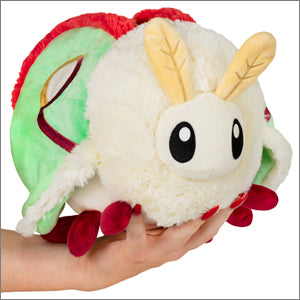 A plush toy resembling a Luna moth with green and red wings, cream-colored body, and black eyes, being held in a person's hand.