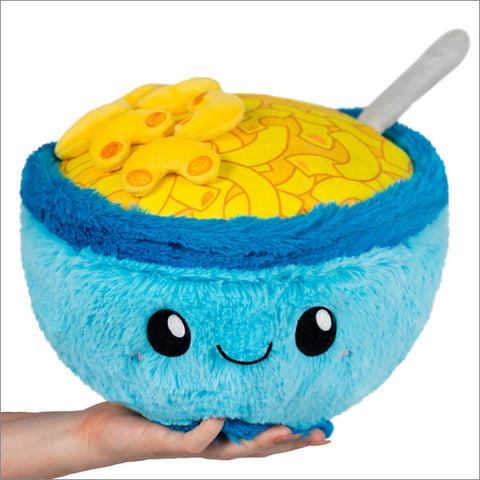 A blue plush bowl with mac & cheese fabric on top. There are several plush macaroni. Held on a hand with a white background.