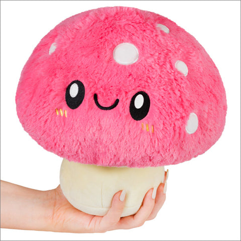 A hand holds a plush pink mushroom with a happy face