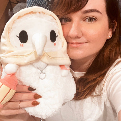 A woman holds the plush Plague Nurse up to her face. It is slightly larger than her head.
