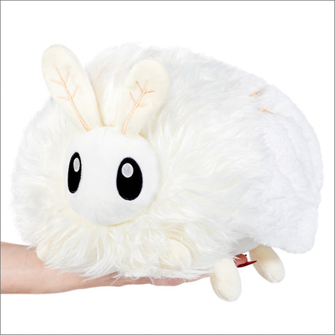 A plush toy resembling a white poodle moth with big eyes, held in someone's hand.