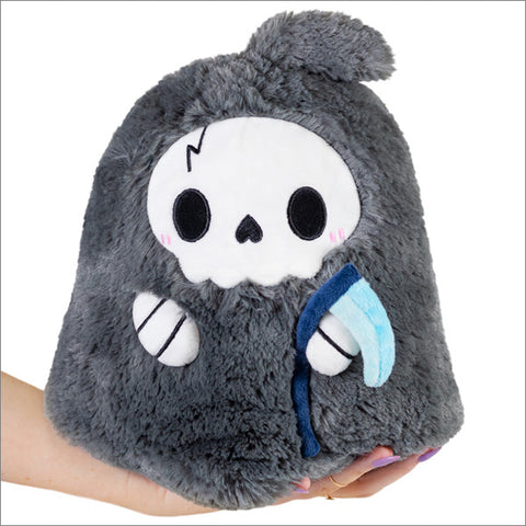 A grey plush reaper toy with a white mask and blue scythe held in someone's hand