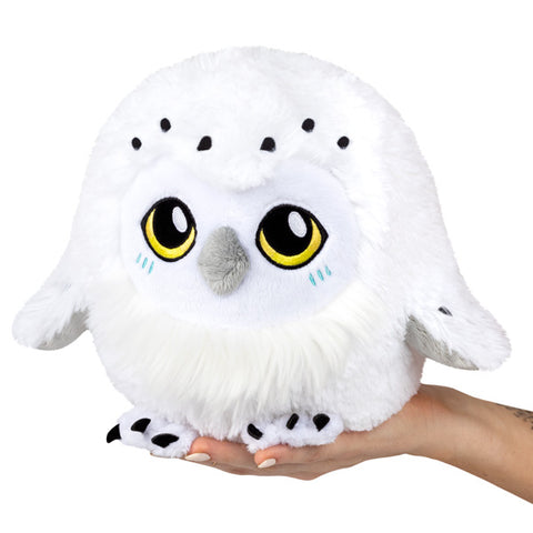 A plush snowy owl with large yellow eyes held in someone's hand