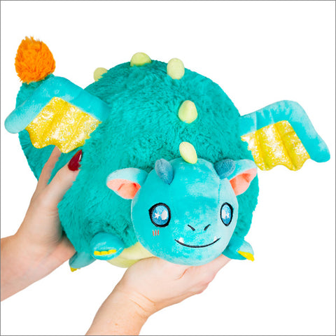 A turquoise plush dragon with yellow wings, belly, and spikes. It is held in two hands.