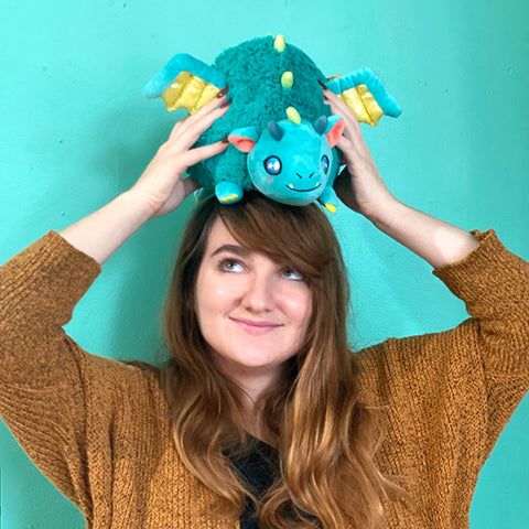 A woman balances the plush dragon on her head. It is slightly larger than her head.