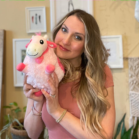 A woman holds the plush strawberry cow. It is slightly larger than her head.