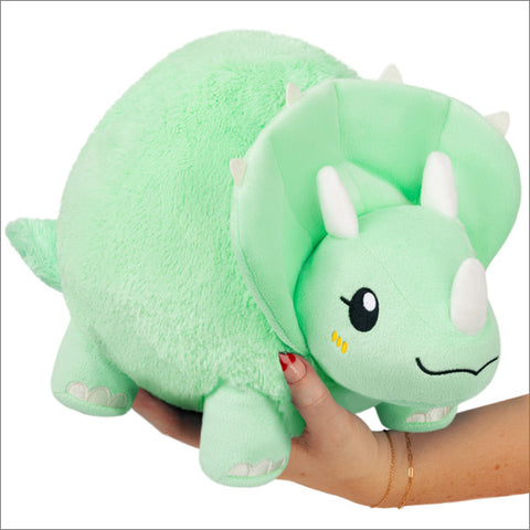 A mint green plush Triceratops is held on someone's hand