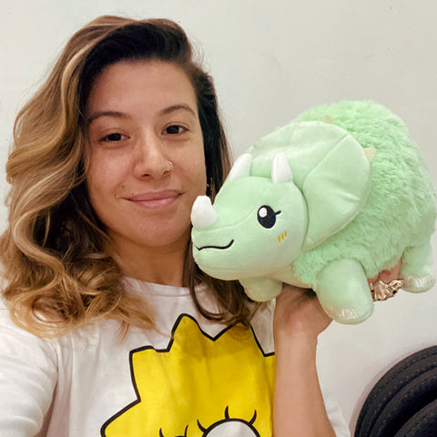 A woman holds the plush Triceratops near her face. It is slightly larger than her head.