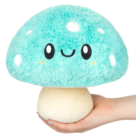 A plush turquoise mushroom with a happy face, held in someone's hand.