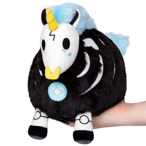 A plush skeleton-themed unicorn. It has a black and white body, light blue mane and tail, yellow horn and nose ring. It is held in someone's hand.