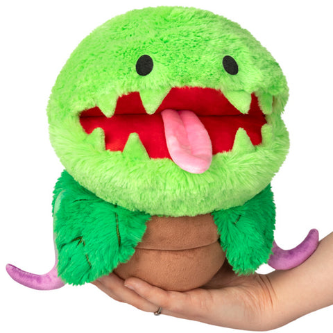 A plush toy resembling a Mini Venus Fly Trap with a green head, red mouth and tongue, and brown body.