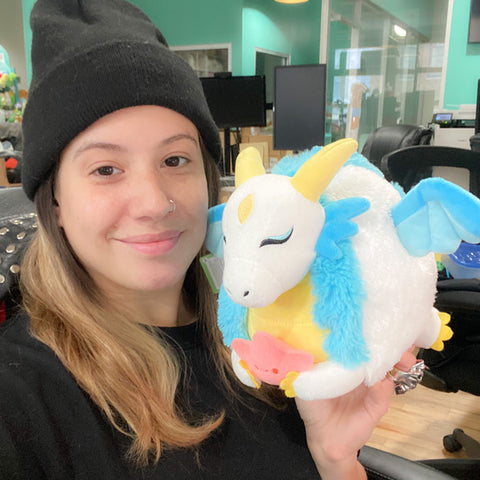 A woman holds the plush dragon up to her face. It is slightly larger than her head.