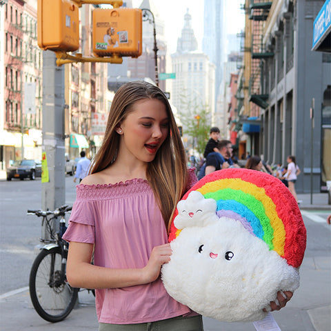 A young woman holds the plush rainbow. It is about the size of her torso.