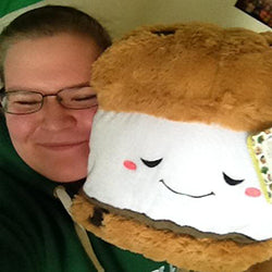 A woman holds the plush s'more up to her face. It is significantly larger than her head.