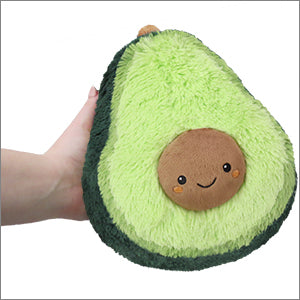 A hand holds a plush avocado with a smiley face on a white background