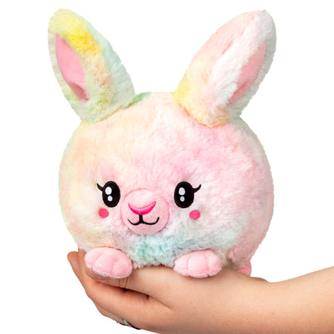A plush toy resembling a pastel tie-dye bunny with big eyes and fluffy texture, being held in a person's hand.