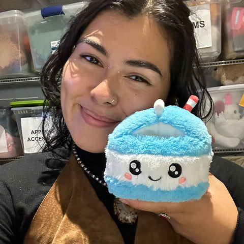 A woman holds the plush milk carton up to her face. It is slightly smaller than her head.