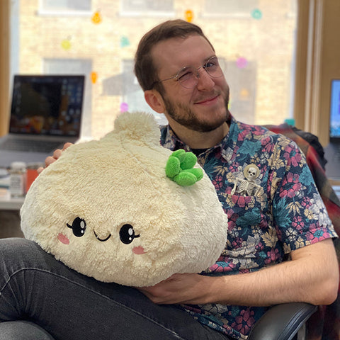 A man holds the plush soup dumpling. It is about the size of his torso.