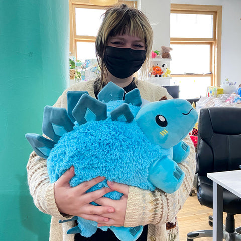 A woman holds the plush stegosaurus. It is about the size of her torso.